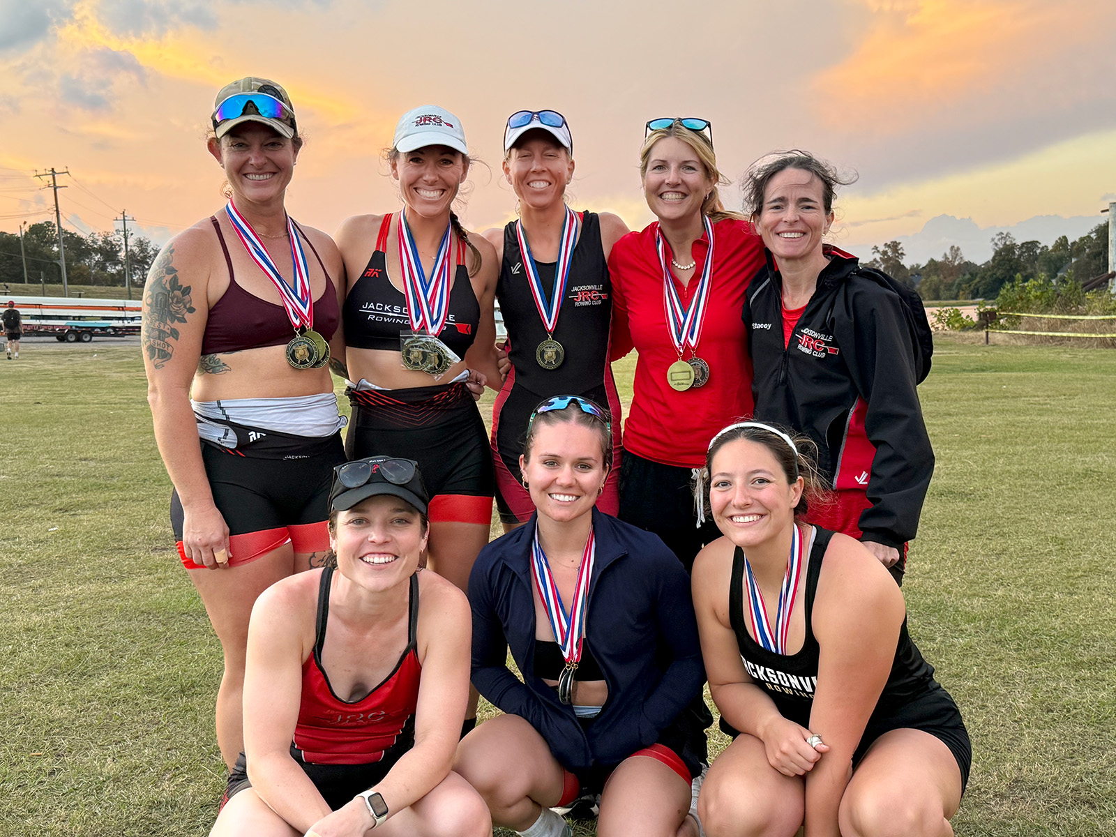 JRC racers posing for a group shot in front of their trailer loaded with rowing shells